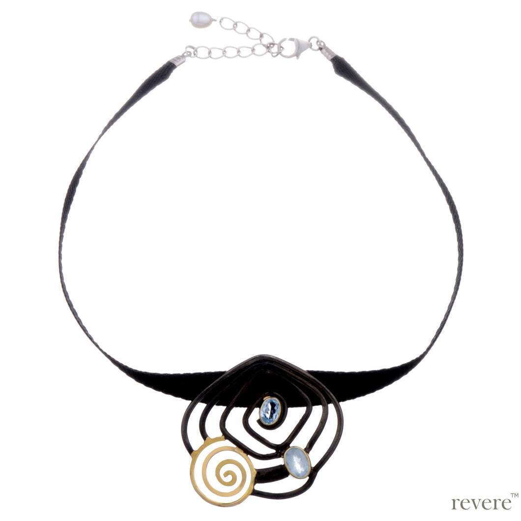 Neckpiece is a black ribbon choker with a hand made concentric oxidised and gold plated sterling silver pendant embellished with blue topaz ending with two inch sterling silver adjustable.